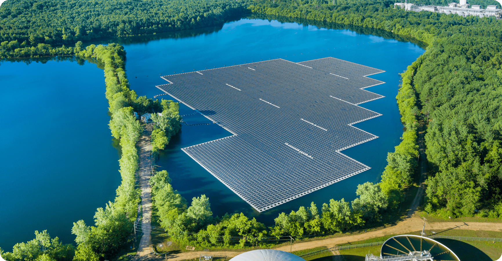 Una gran instalación de paneles solares sobre un lago tranquilo rodeado de árboles verdes, destacando las soluciones de energía sostenible.