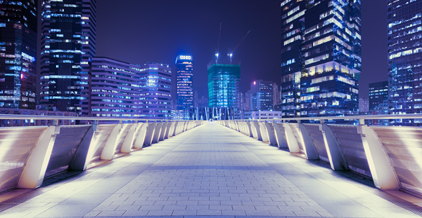 A peaceful walkway in front of a city skyline at night, with soft lights casting a warm glow on the path.
