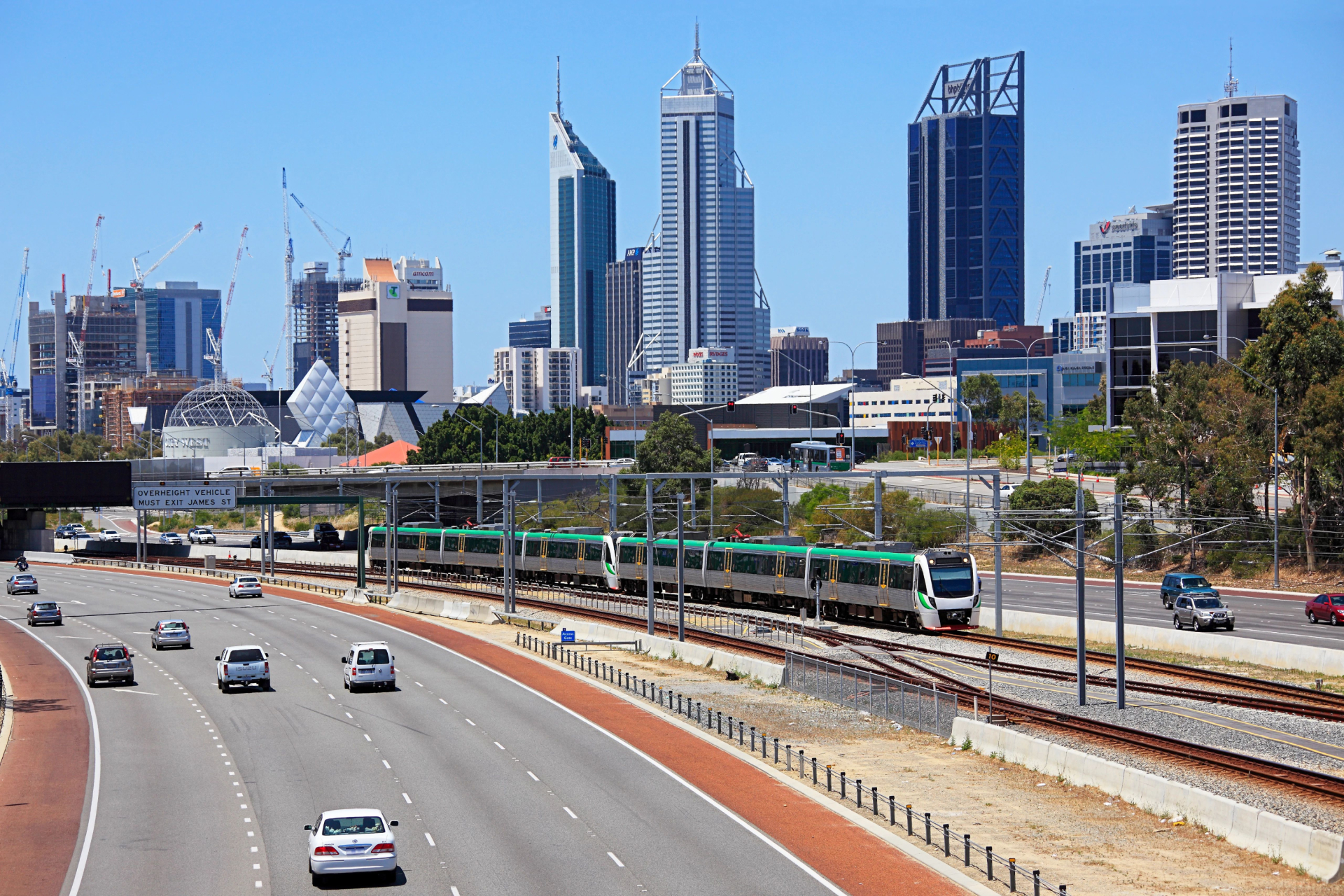 A locomotive traveling along the railway, passing through a scenic landscape, with cars driving along the highway.