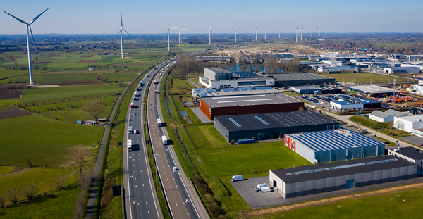 A vast industrial landscape featuring multiple wind turbines alongside a busy highway.