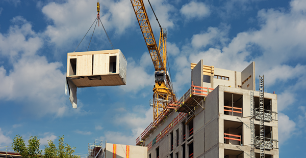 Sur un chantier de construction, une grue jaune empile des matériaux de construction pour un développement résidentiel.