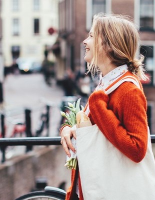 Verstedelijking in Nederland – Een integrale aanpak voor duurzame verstedelijking is de uitdaging Vrouw met tas over schouder en bos tulpen lopend over brug van Amsterdamse grachten