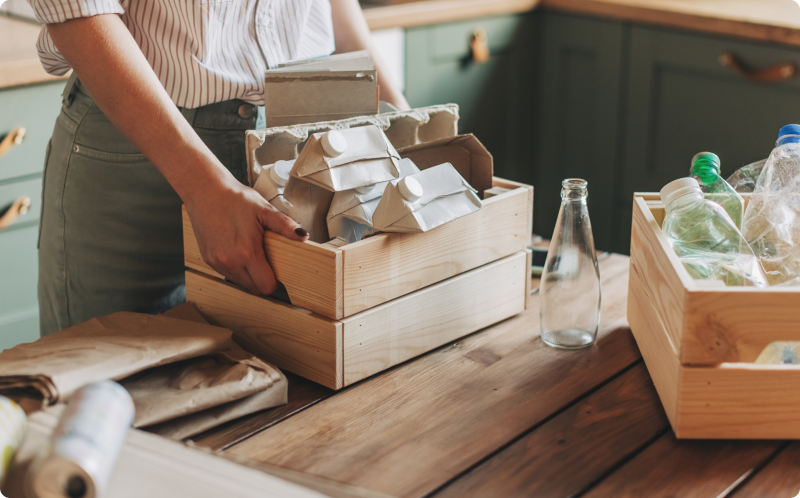 Young woman standing at the table in the kitchen and segregating waste to correct containers