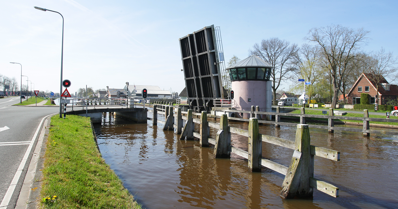 A bridge spans a tranquil canal, connecting both sides with a clear blue sky above.