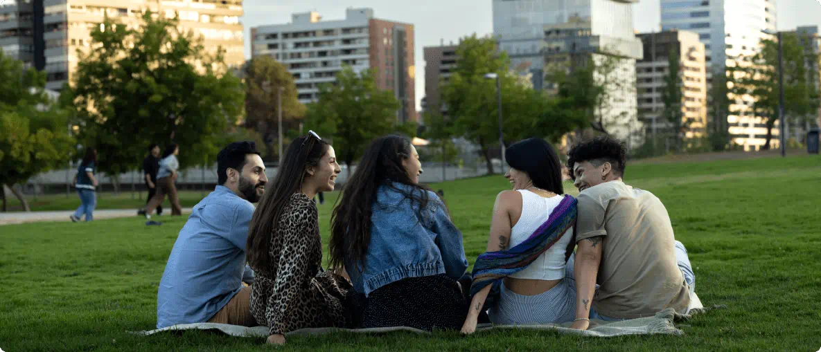 Friends gathered on the grass in a park, sharing smiles and conversation on a bright, sunny day.