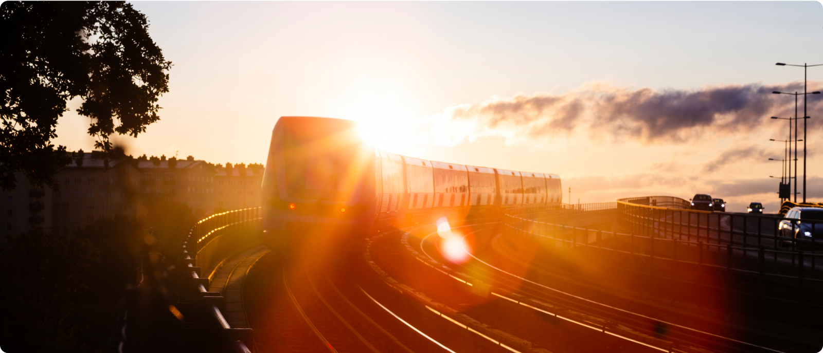 A train journeys down the tracks, framed by a stunning sunset that casts a golden glow over the landscape.