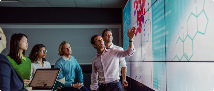 A group of individuals observing a large screen displaying various graphs and data visualizations.