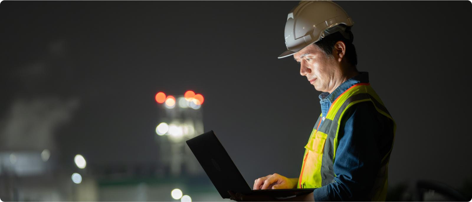 A man in a hard hat and safety vest engages with a laptop, highlighting the integration of safety and digital tools in construction.