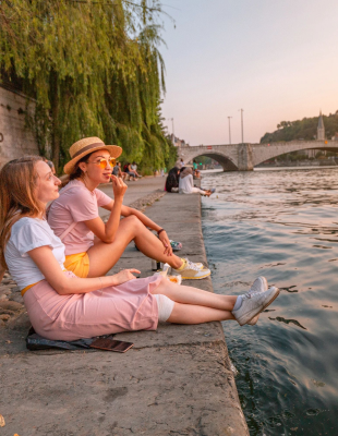 Three girls sitting on the riverbank, enjoying the view and the tranquility of the flowing water.