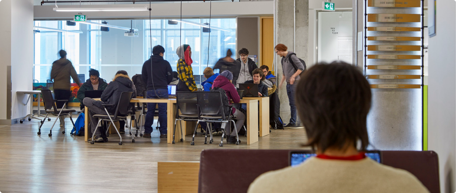 People engaged in work at tables in a spacious area, utilizing computers for various tasks and activities.