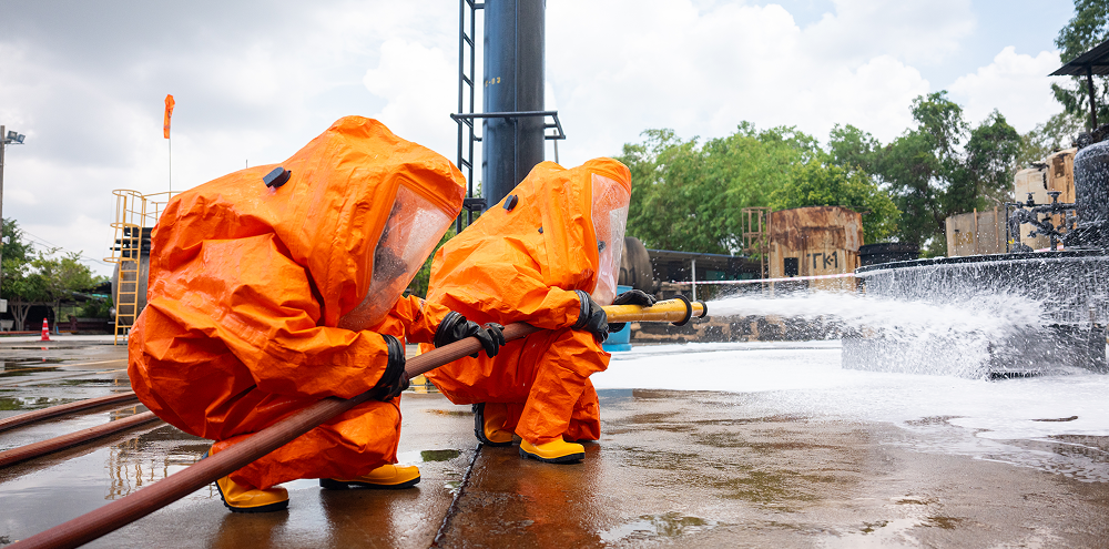 Two people dressed in orange suits are spraying water on a concrete surface, likely for cleaning or cooling purposes.