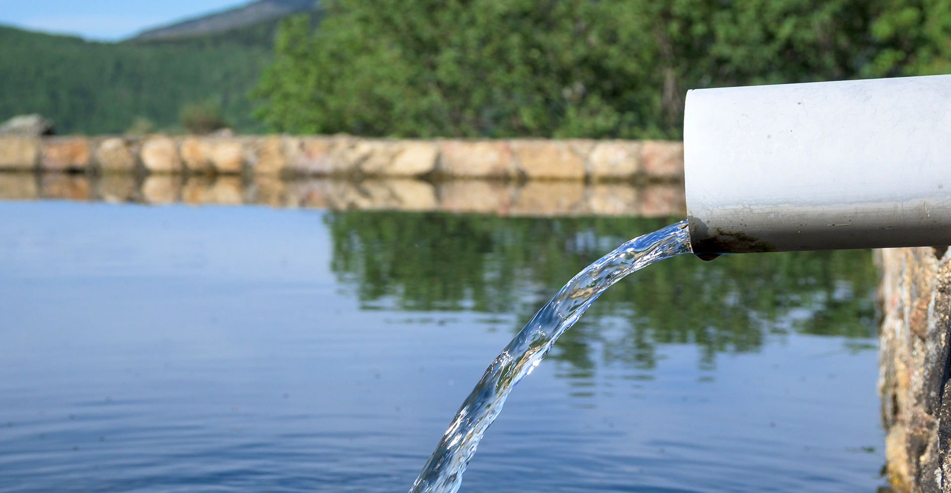 Water flows from a pipe into a tranquil lake, enhancing the natural scenery.