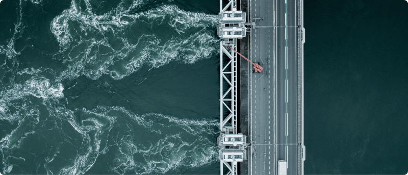 Aerial view of a bridge spanning over a serene body of water, showcasing its architectural design and surrounding landscape.