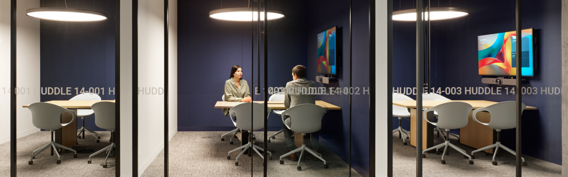 Two people sitting at a table in a conference room, contributing to a professional discussion or presentation.