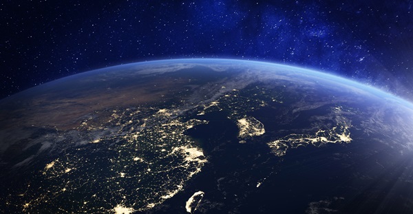 Night time view of Earth with glowing city lights and starry sky.