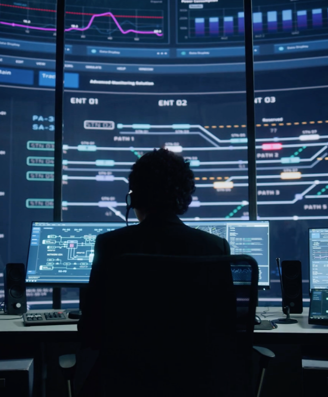 An individuals sitting at computers, engrossed in work, with a sizable screen displaying information.