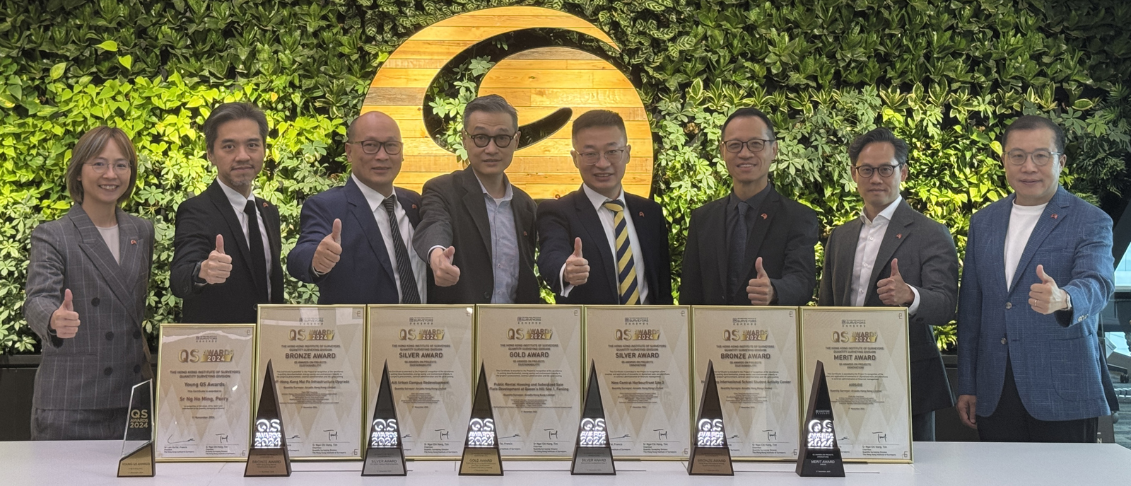 A group of professionals stands together in front of a wall displaying numerous awards, showcasing their achievements and accomplishments.