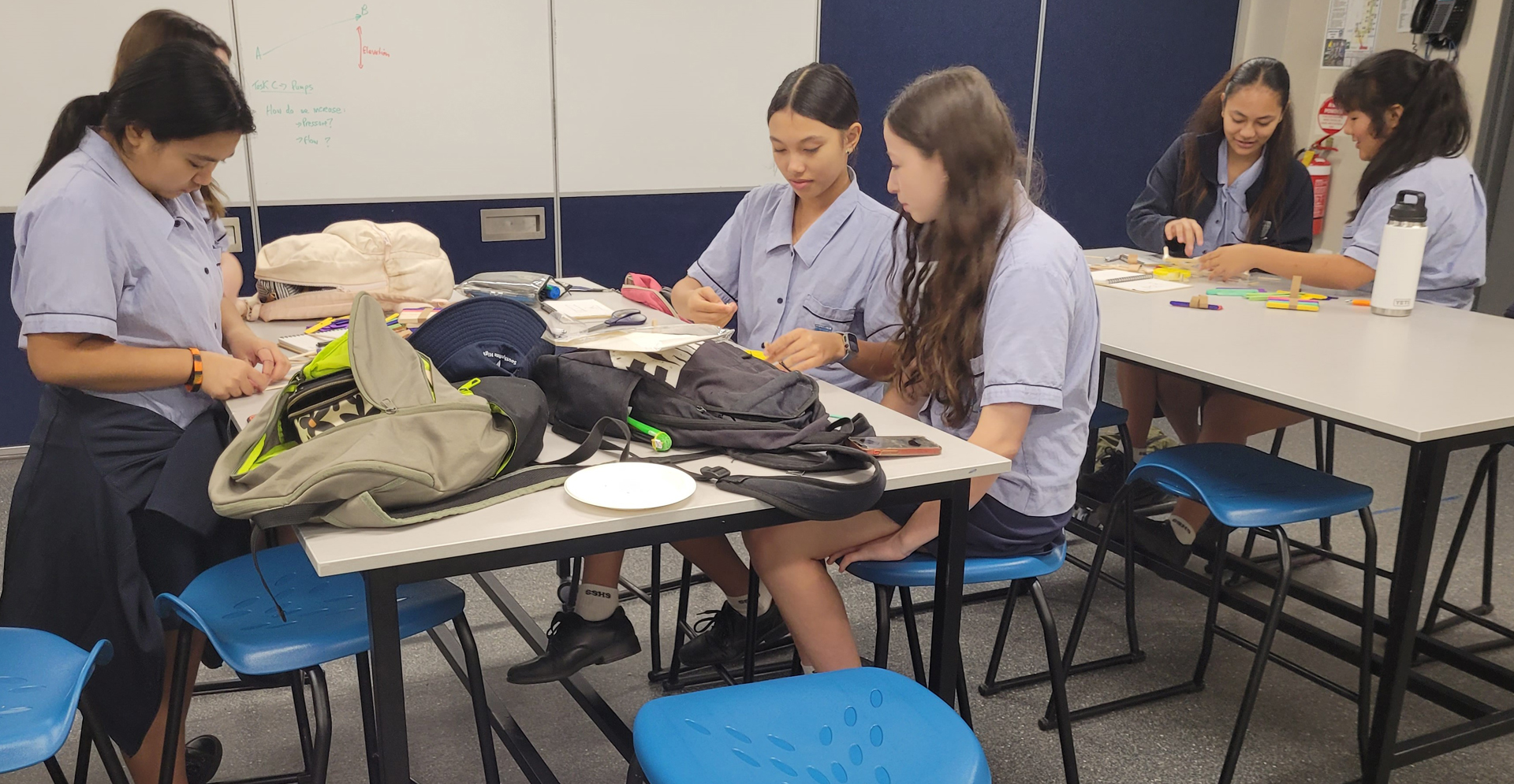 A diverse group of students engaged in learning, sitting at tables in a classroom setting.