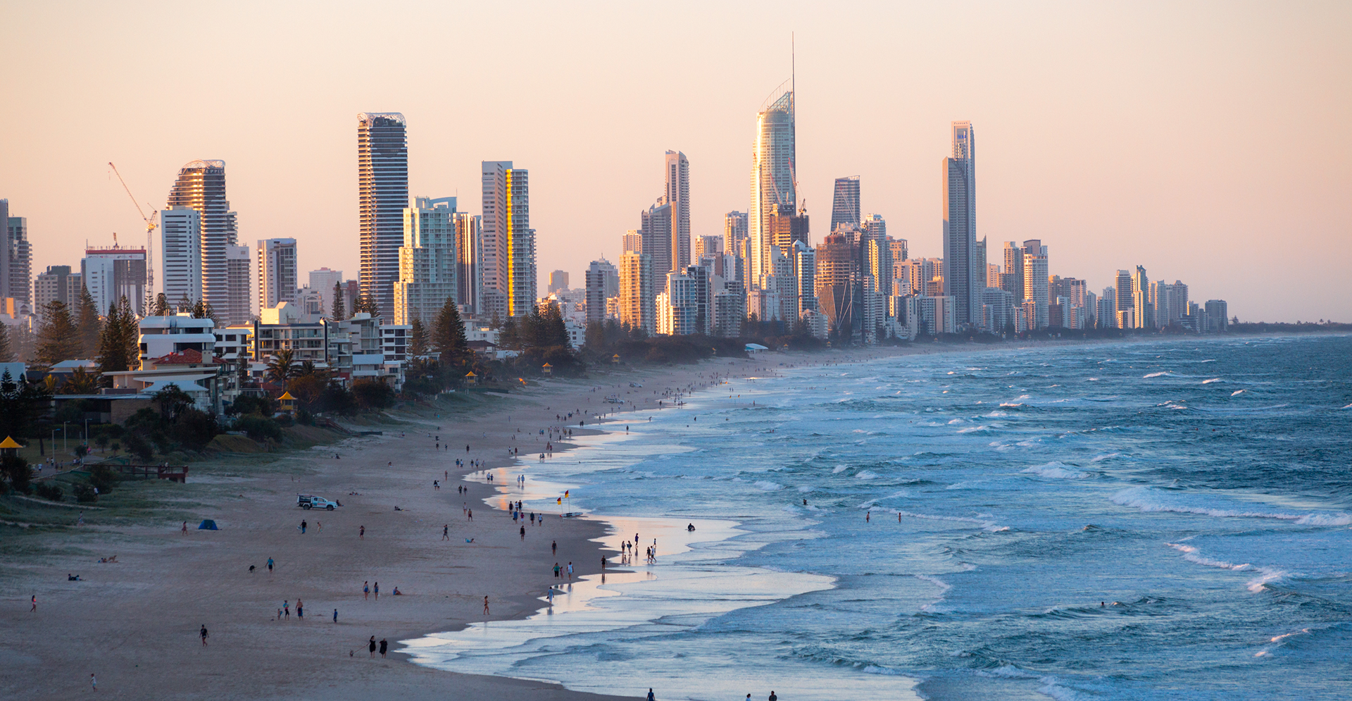 A lively beach populated with individuals relaxing on towels, children playing in the sand, and others swimming in the ocean.