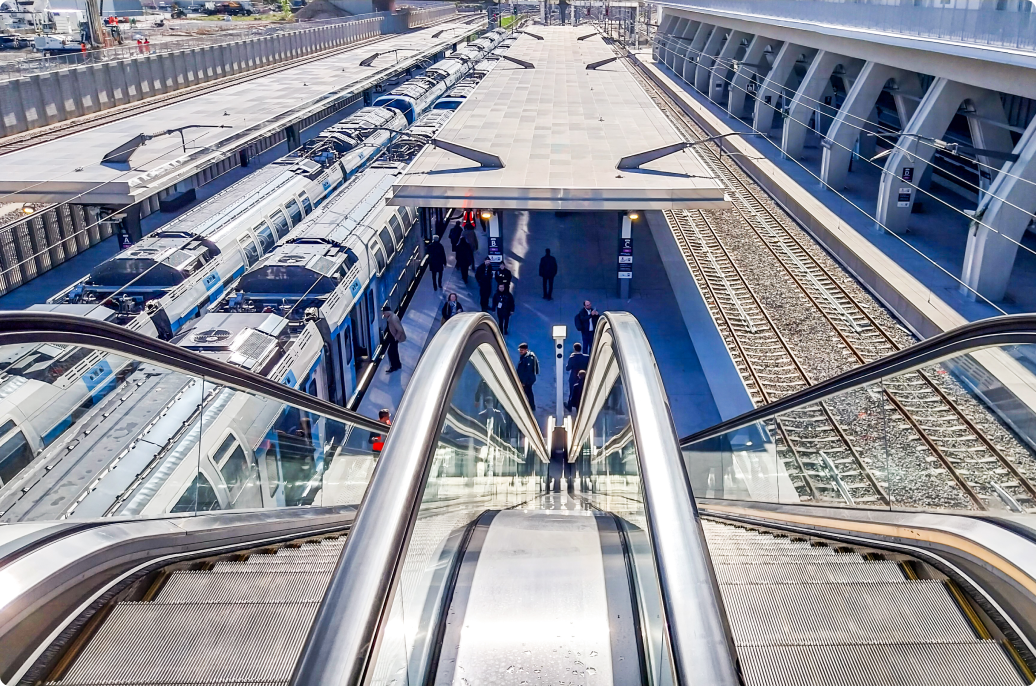 An escalator at a train station, flanked by two trains, illustrating the bustling transit environment. 