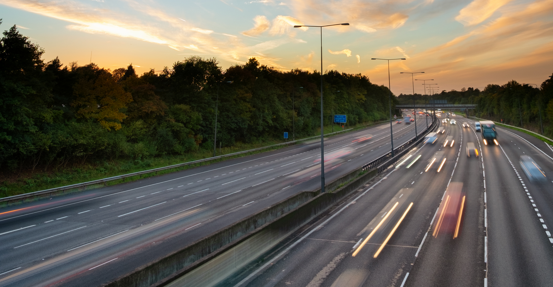 A highway at sunset with cars driving, casting long shadows and vibrant colors across the sky.