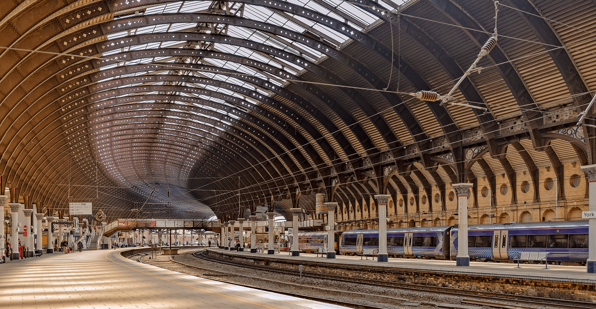A train station featuring a train on the tracks, with platforms and signage visible in the background.