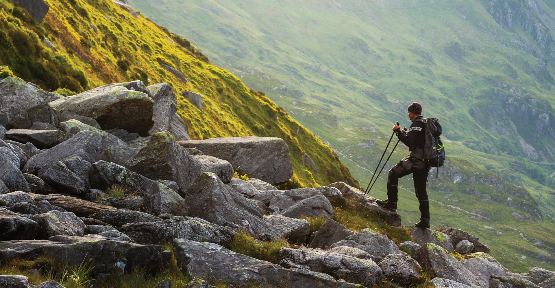 A hiker with a backpack ascending a mountain path, with a scenic view of the landscape in the background.