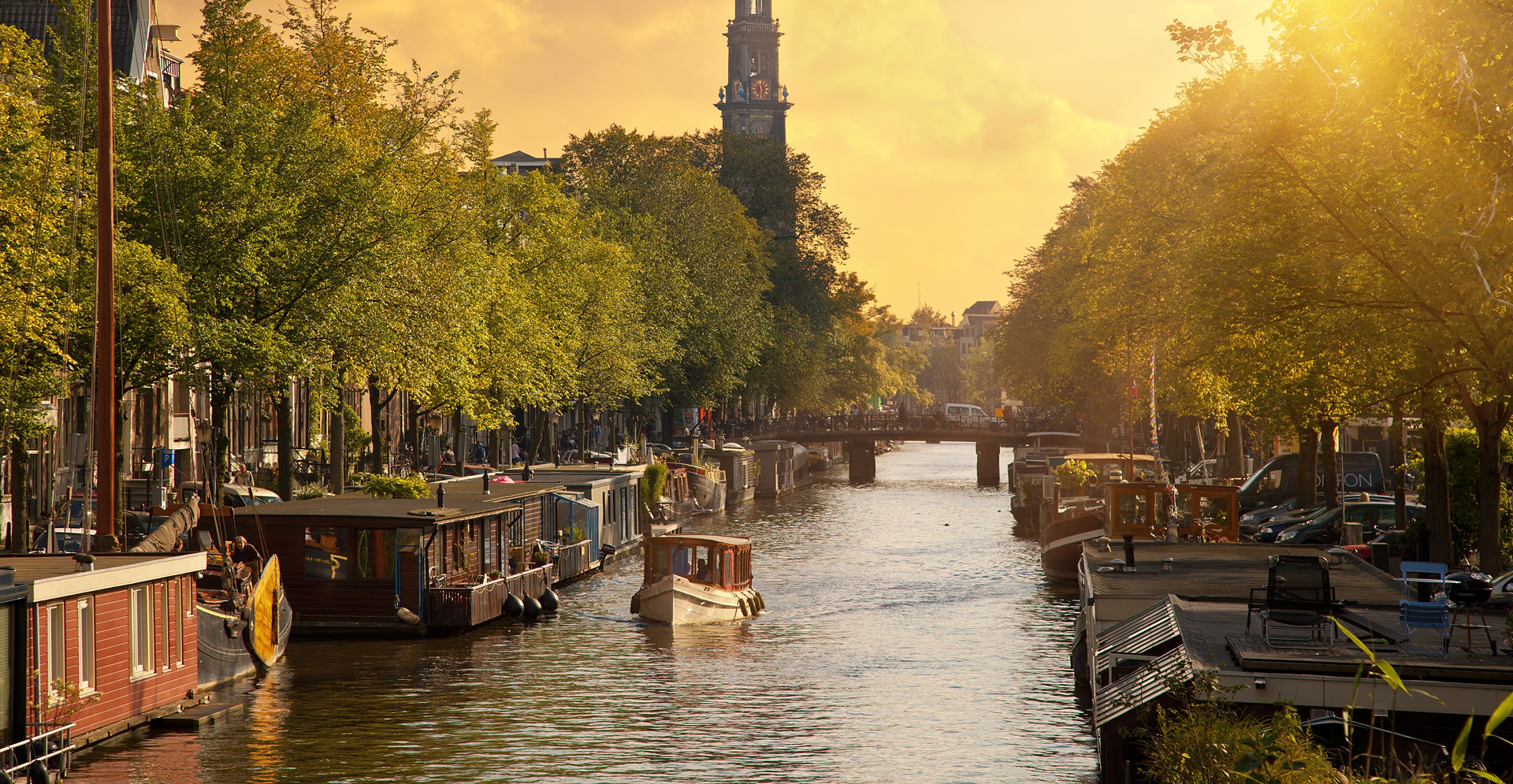Canal in Amsterdam with the church 'Westerkerk' lined with boats gently floating on the water.