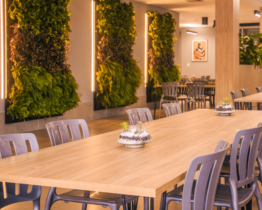 Dining area with tables and chairs against a plant-covered wall.