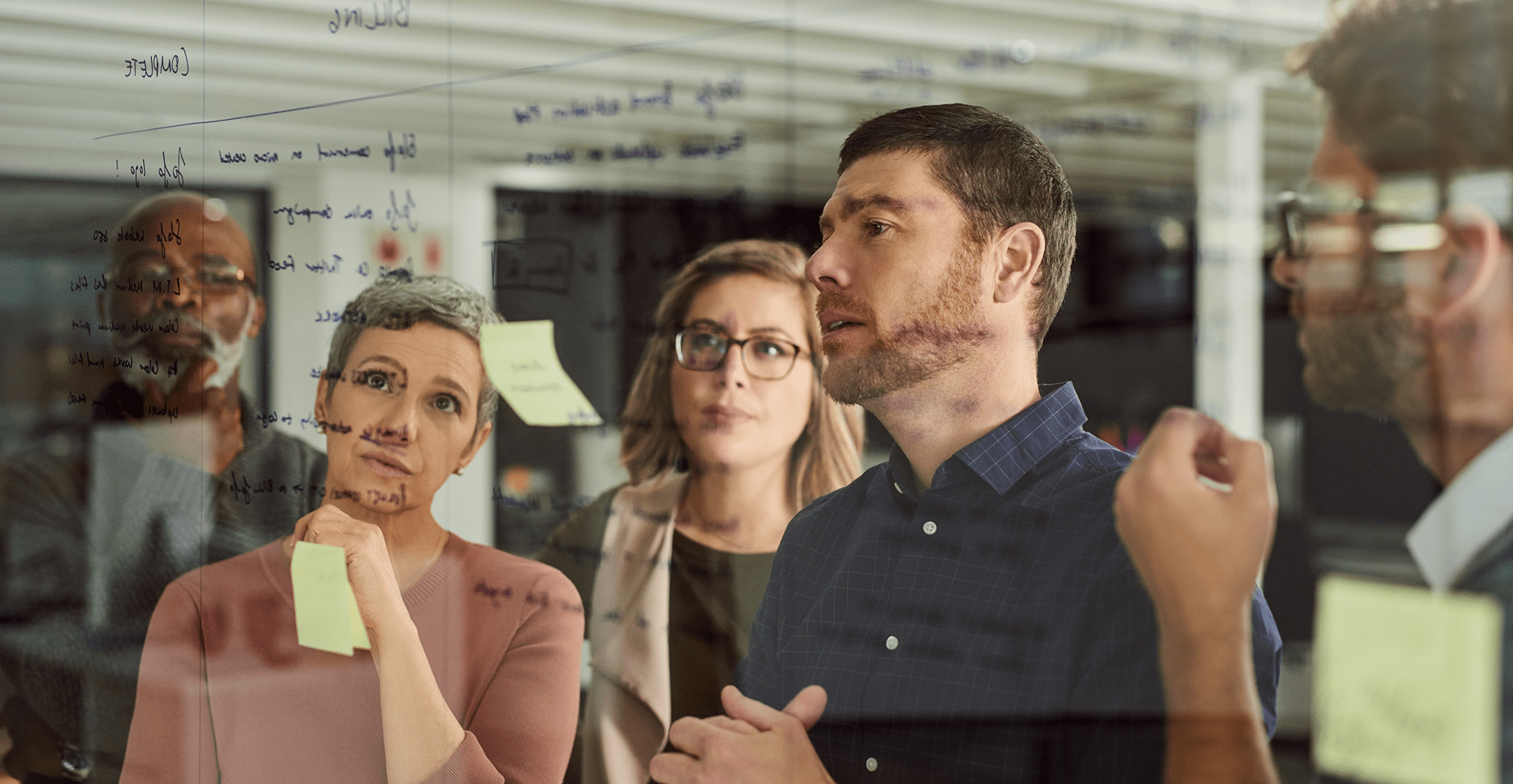 A team of people focused on a board adorned with sticky notes, brainstorming and strategizing together.