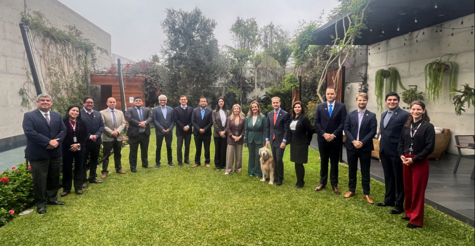 A group of professionally dressed individuals in suits and ties standing together in a lush garden setting.