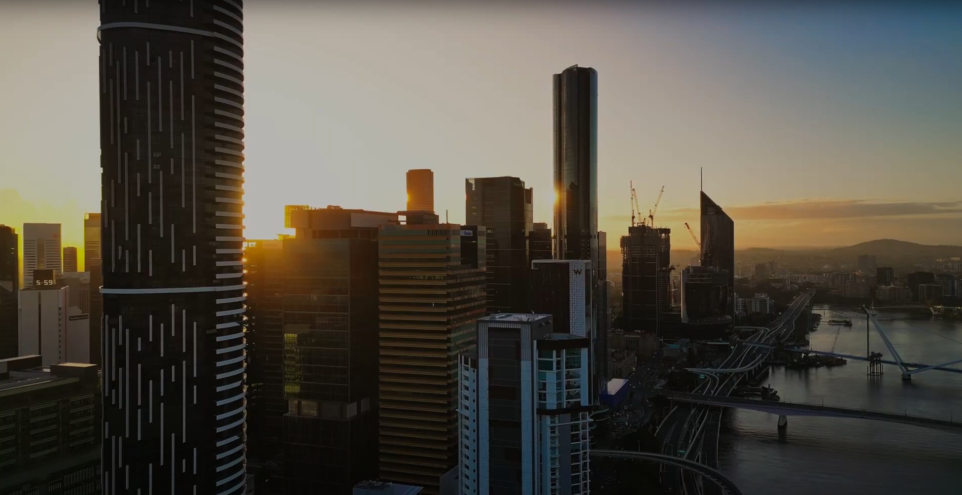 A city skyline at sunset, featuring tall buildings silhouetted against a vibrant orange and purple sky.