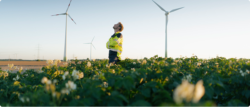 A person is seen in a field filled with green plants, enjoying the natural landscape under bright daylight.