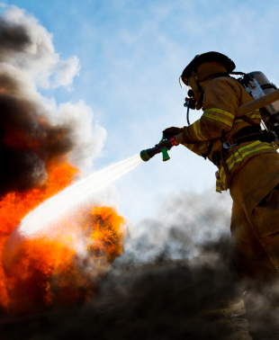 A fireman extinguishes flames by spraying water from a hose, demonstrating bravery and commitment to safety.