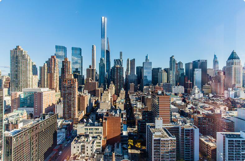 The city skyline viewed from a high-rise, featuring a mix of modern skyscrapers and urban architecture under sunlight.
