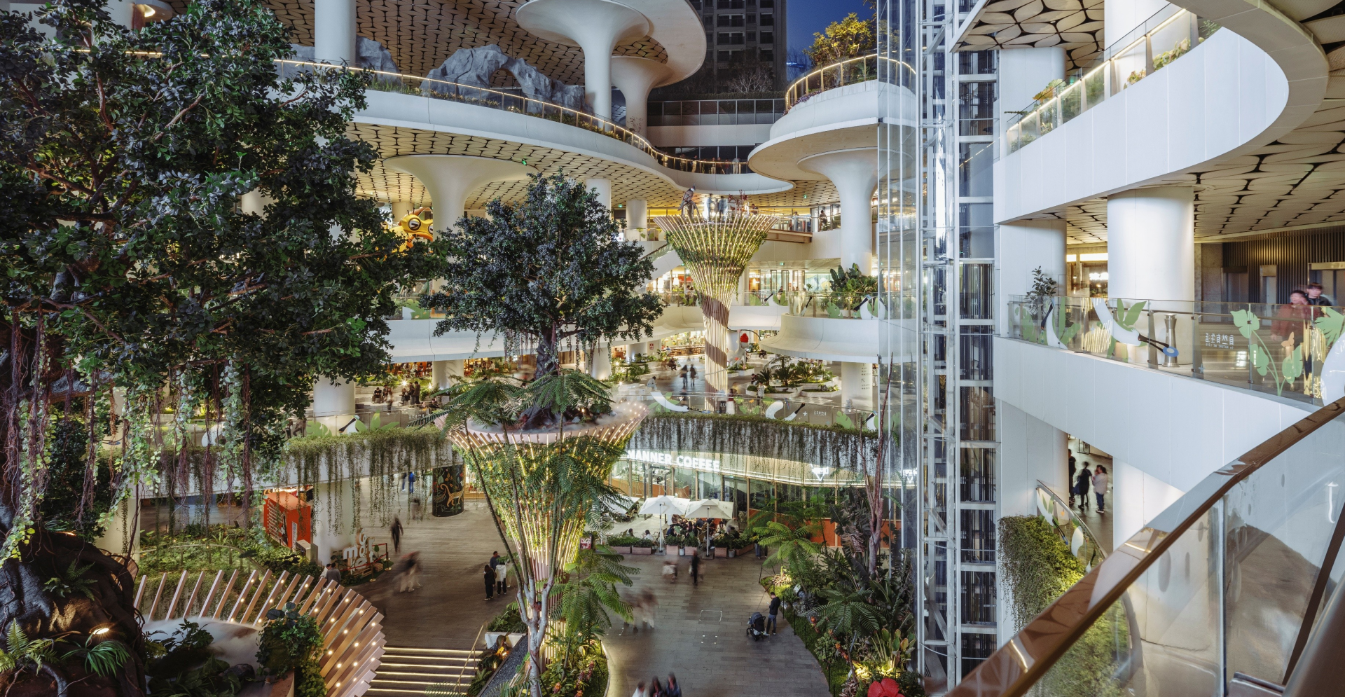The atrium features lush trees and plants, creating a vibrant indoor garden atmosphere within the building.