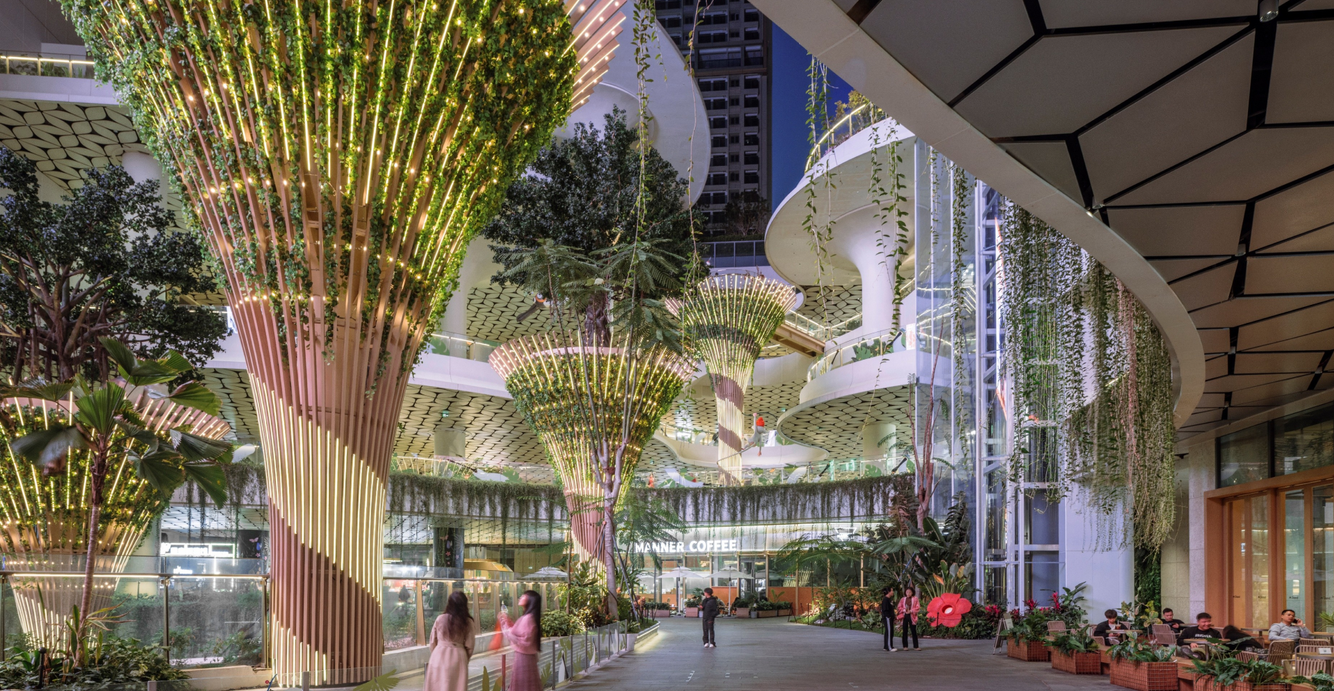 The atrium features lush trees and plants, creating a vibrant indoor garden atmosphere within the building.