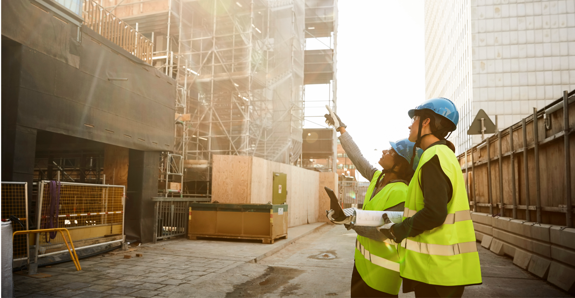 Two construction workers in hard hats stand in front of a partially constructed building, discussing their next steps.