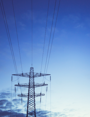 High voltage power lines and electricity towers silhouetted against a clear blue sky, showcasing energy infrastructure.