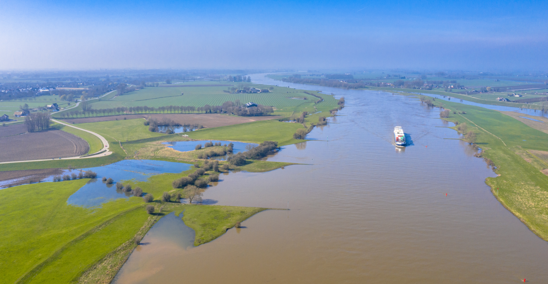 Scenic view of a boat sailing down a tranquil river, with trees lining the banks under a sunny sky.