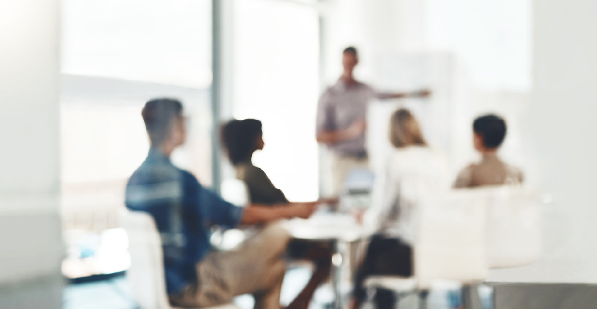 Geblurde foto van mensen in een kantooromgeving die aan het kijken zijn naar iemand die uitleg geeft.