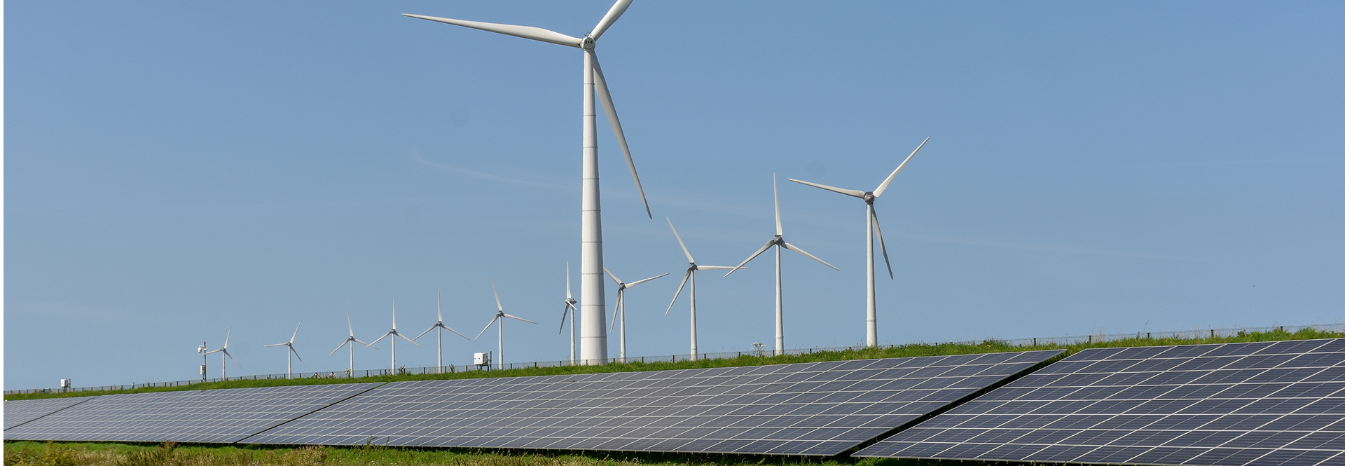 Solar panels and wind turbines stand in a grassy field, showcasing renewable energy sources in a natural landscape.