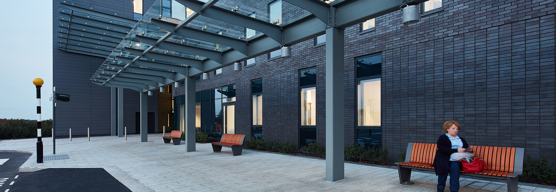 A woman seated on a bench in front of a building, enjoying the outdoors in a serene environment.