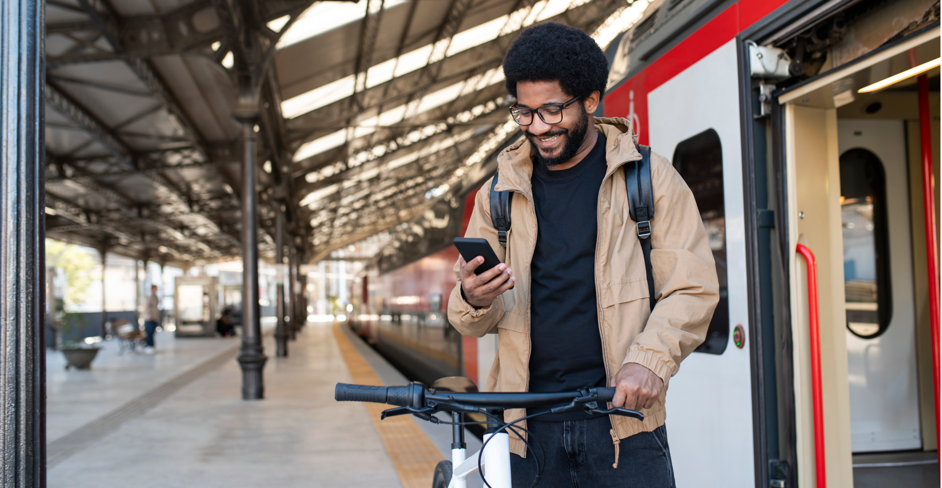 Smiling man using mobile phone standing by bicycle near train at station
