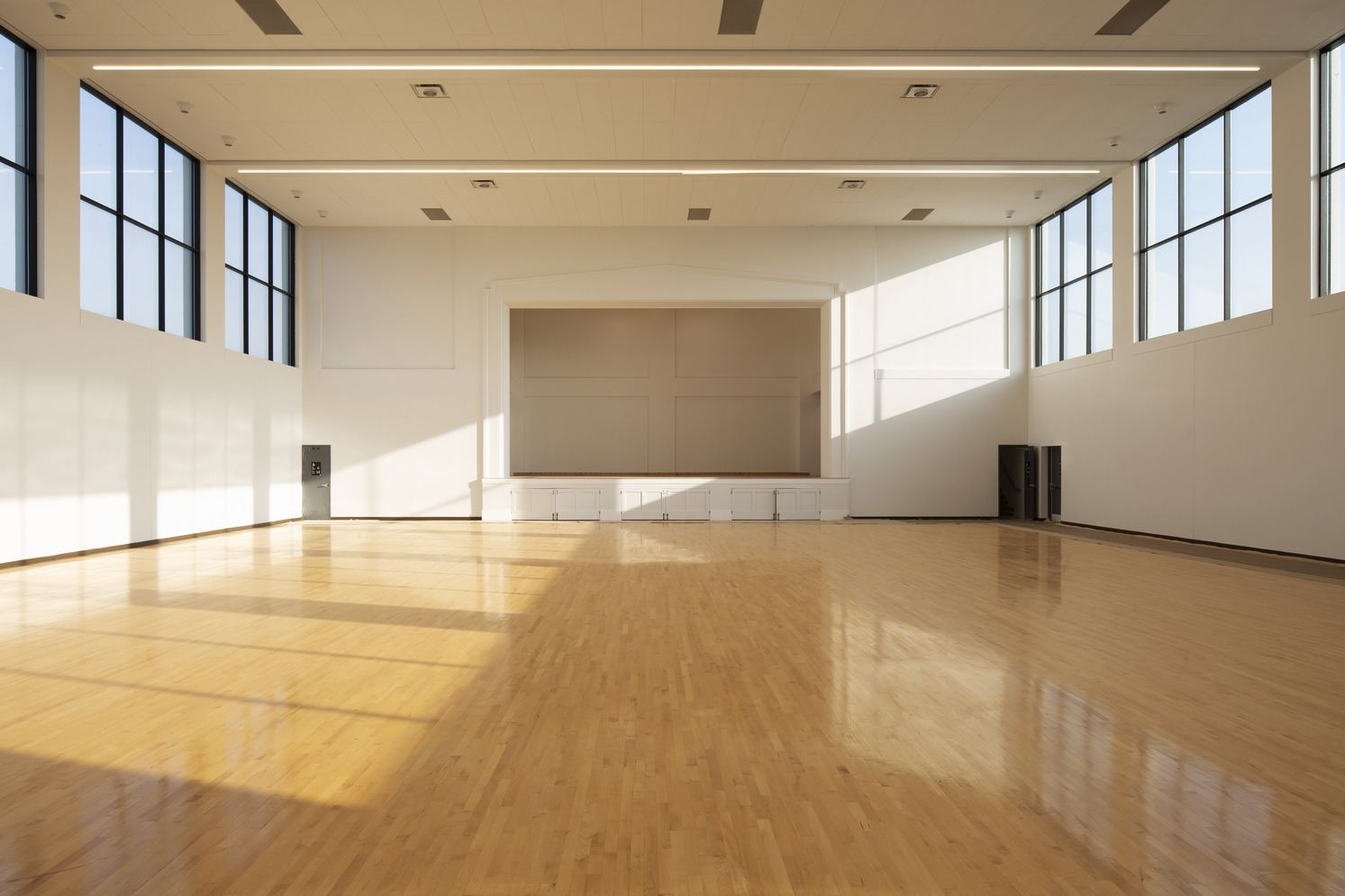 Large empty room featuring hardwood floors and multiple windows allowing natural light to enter.