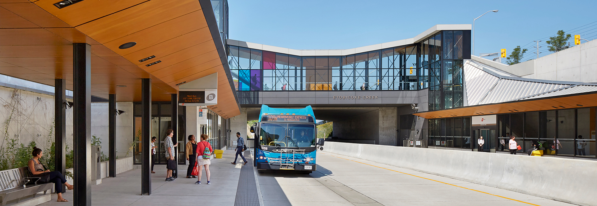 A bus is parked at a bus stop adjacent to a building, ready to pick up passengers.