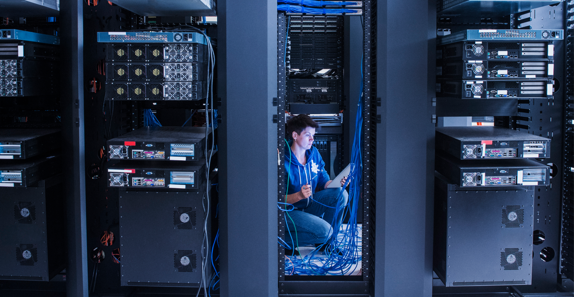 A woman sitting in a server room filled with multiple servers, concentrating on her work in a modern data center.
