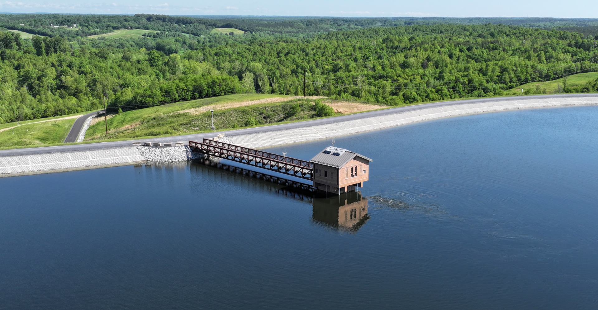 A dam on a serene lake, encircled by lush green trees, reflecting nature's tranquility.