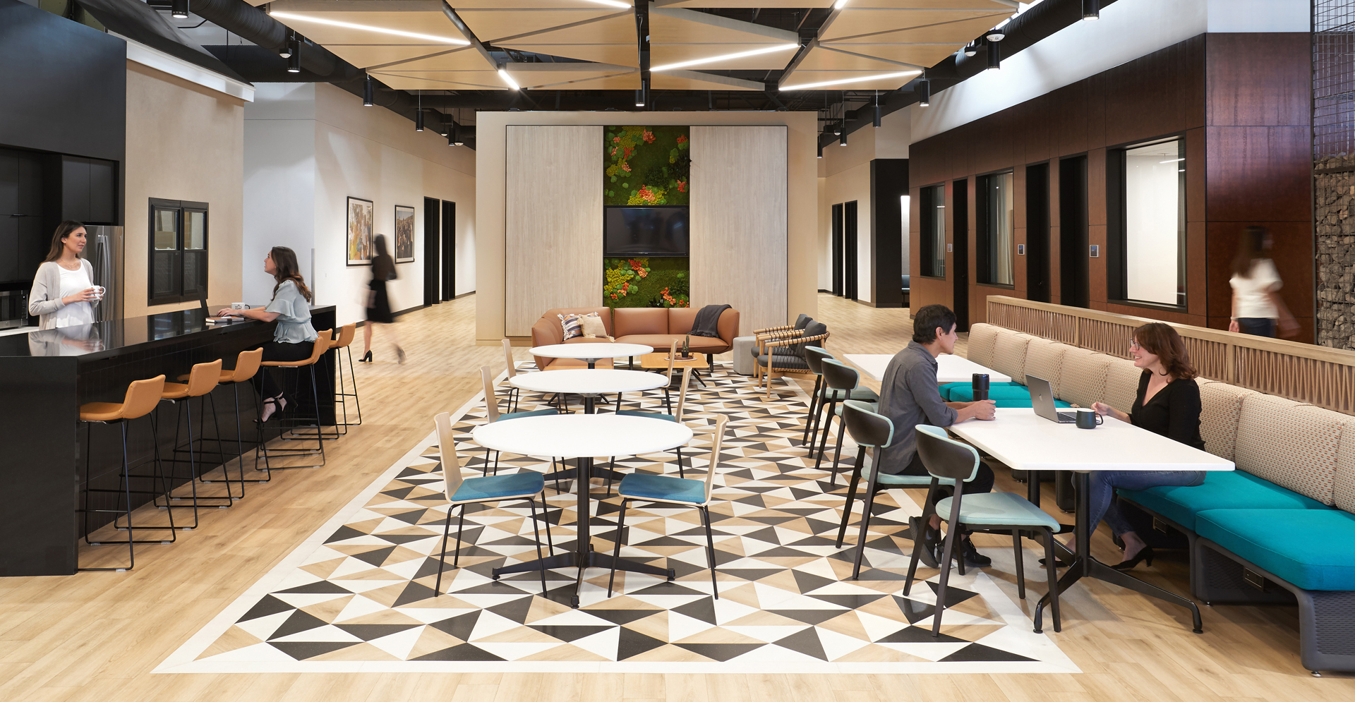 The bustling lobby of a contemporary office building, filled with individuals seated at tables, engaged in various tasks.